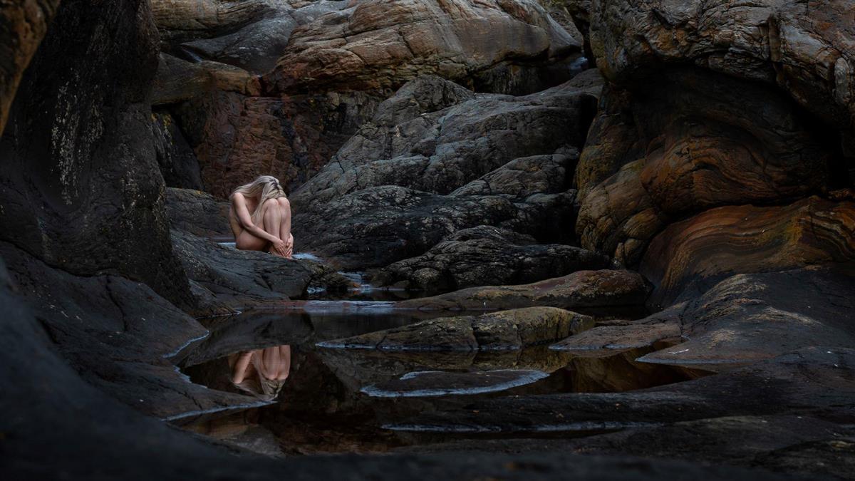 Foto av naken jente sittende i steinlandskap. - Klikk for stort bilete