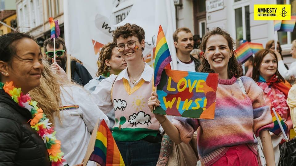 unge mennesker i pride parade med regnbueflagg og plakat med teksten love wins