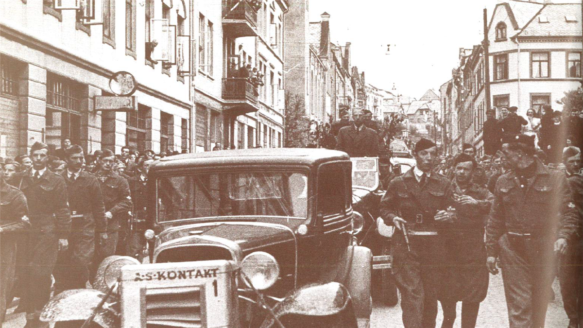 Gammelt fotografi med en bil og mennesker i gatene i Ålesund under andre verdenskrig - Klikk for stort bilete
