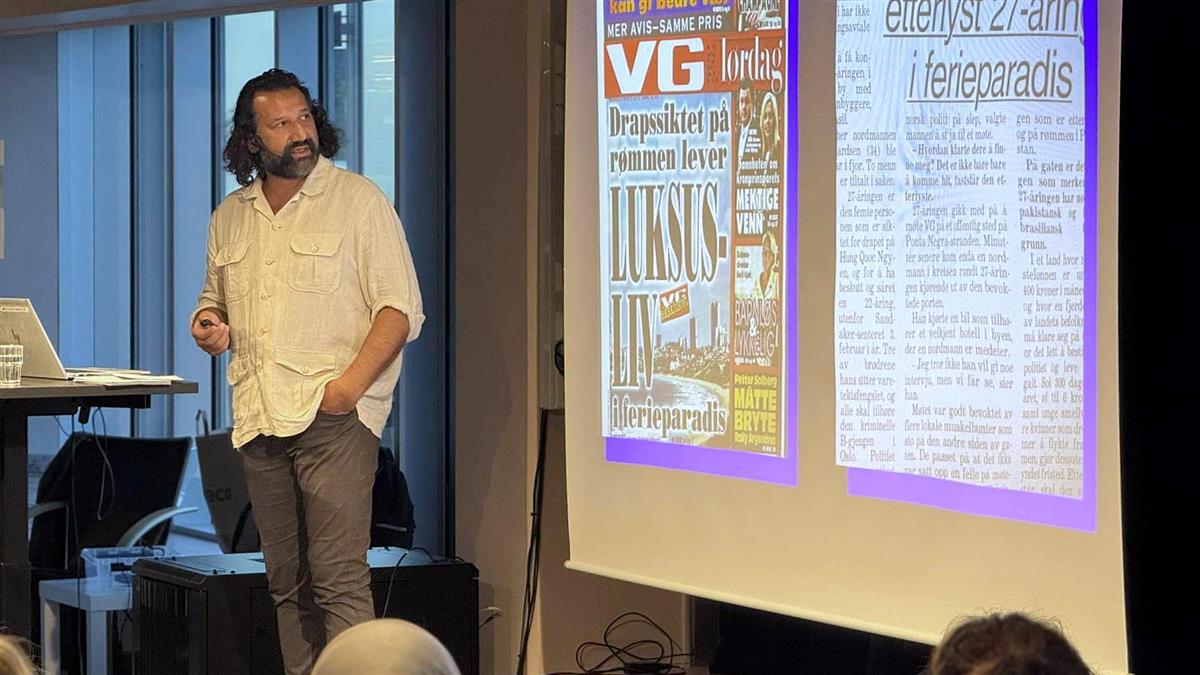 Kadafi Zaman på scenen foran et lerret. På lerret ser vi projisert to avisutklipp, det ene fra VG. - Klikk for stort bilete