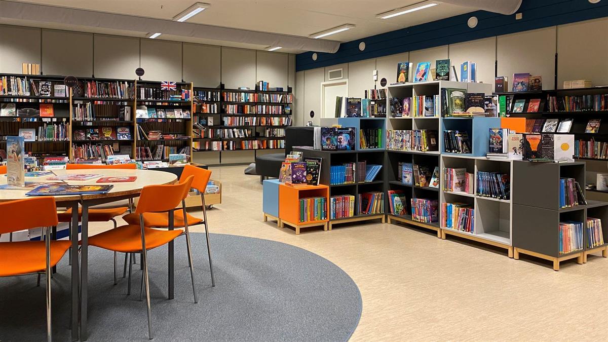 Bord, stolar og mange bokhyller med bøker for barn og unge. Foto. - Klikk for stort bilete